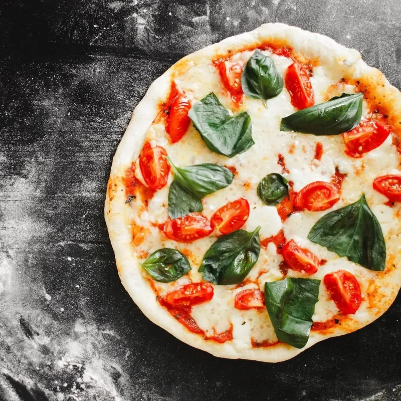 A margherita pizza with cherry tomatoes and basil on a dark floured stone