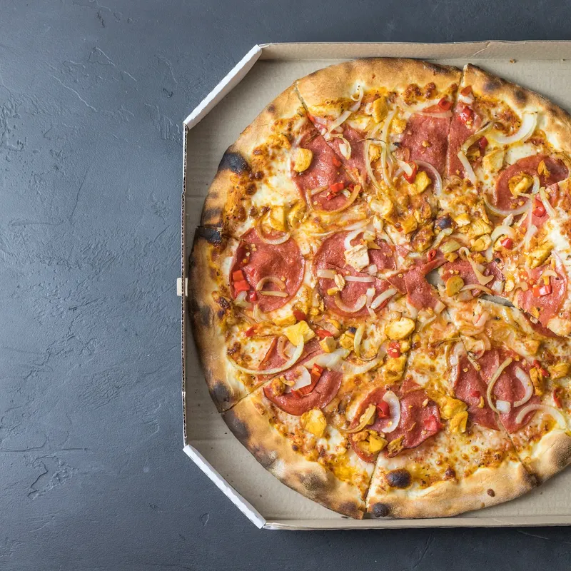 A hand lifting a slice from a pizza in an open delivery box